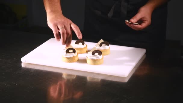 Chef décore gâteau au dessert. Gros plan sur la touche finale. L'homme tend des confiseries. Suspendez des cupcakes au chocolat avec de la crème. Confiseur délicatement et soigneusement décoré avec des confiseries — Video