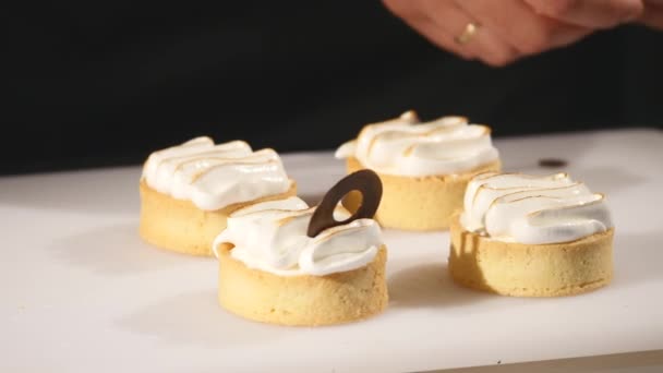 Chef décore gâteau au dessert. Gros plan sur la touche finale. L'homme tend des confiseries. Suspendez des cupcakes au chocolat avec de la crème. Confiseur délicatement et soigneusement décoré avec des confiseries — Video