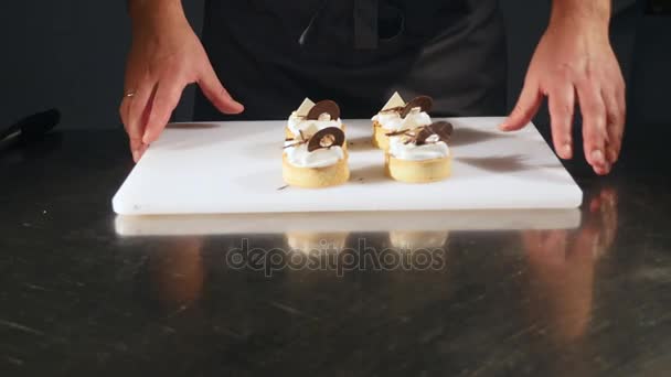 Chef decora pastel de postre. Primer plano de los toques finales. Hombre manos confitero. Cuelga las magdalenas de chocolate con crema. Pastelero suavemente y cuidadosamente decorado con confección — Vídeo de stock