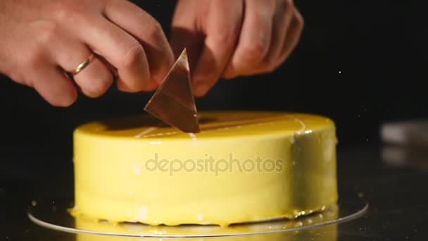 Detalhes do bolo. Chocolate e pretzels. Bolo acabado de cozinhar. Confeiteiro gira o bolo e decorá-lo. Bolo de creme amarelo com cobertura de chocolate, chocolate e pretzels. Confeiteiro decorar um — Vídeo de Stock