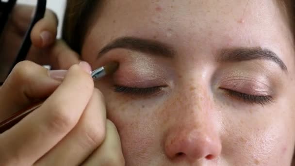 Genç profesyonel kadın photomodel çehresini Güzellik Salonu Makyaj süreci sırasında kapatın. Genç visagiste özel fırça kullanarak göz kapağı üzerinde göz farı uyguluyor — Stok video