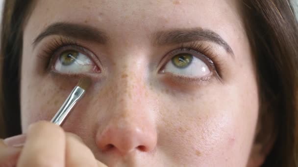 Κοντινό πλάνο του προσώπου των νέων επαγγελματική γυναικεία φωτομοντέλο κατά τη διαδικασία του μακιγιάζ στο κατάστημα ομορφιάς. Νέοι visagiste είναι η εφαρμογή eyeshadow στο βλέφαρο με ειδικό πινέλο — Αρχείο Βίντεο