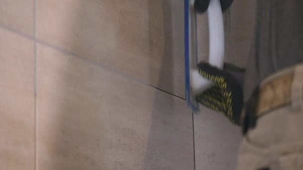 Чоловік вручну кладе шви бежевої плитки на стіну. Близько. повільний рух — стокове відео