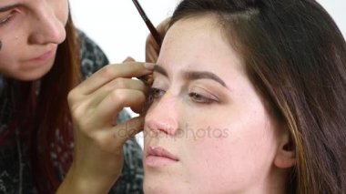 Genç profesyonel kadın photomodel çehresini Güzellik Salonu Makyaj süreci sırasında kapatın. Genç visagiste özel fırça kullanarak göz kapağı üzerinde göz farı uyguluyor