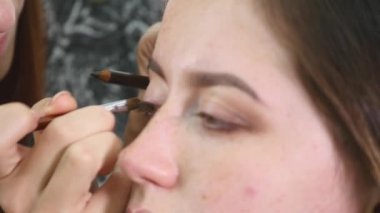 Genç profesyonel kadın photomodel çehresini Güzellik Salonu Makyaj süreci sırasında kapatın. Genç visagiste özel fırça kullanarak göz kapağı üzerinde göz farı uyguluyor