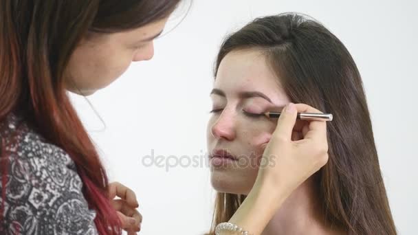 Profesionální vizážistka použití oční stíny na model oka pomocí speciálního štětce. Přírodní make-up v salonu. Krása, make-up a módní koncept