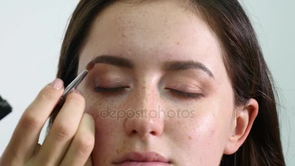 Крупним планом обличчя молодої професійної жіночої фотомоделі під час процесу макіяжу в магазині краси. Молодий візажист наносить повіку за допомогою спеціальної щітки — стокове відео