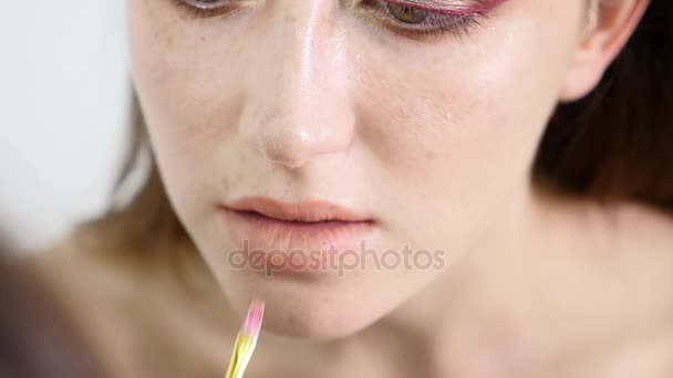 Closeup άποψη του ένας επαγγελματίας καλλιτέχνης μακιγιάζ εφαρμογή κραγιόν στα χείλη μοντέλα που εργάζονται στη βιομηχανία ομορφιά μόδα. Προβολή closeup ενός χεριού καλλιτέχνες χρησιμοποιώντας το ειδικό πινέλο. αργή κίνηση — Αρχείο Βίντεο