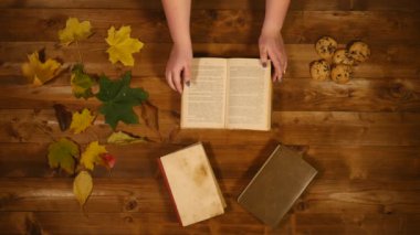 Sonbahar konsepti üstten görünüm. Kitaplar, akçaağaç yaprakları, eski ahşap masa pişirin. Kadın scrolls kitap sayfaları