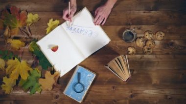 Sonbahar konsepti üstten görünüm. Kitaplar, akçaağaç yaprakları, eski ahşap tabloda çay. Not defterinde yazma kadın