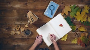 Sonbahar konsepti üstten görünüm. Kitaplar, akçaağaç yaprakları, eski ahşap tabloda çay. Not defterinde yazma kadın