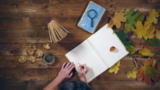 Conceito de outono vista superior. Livros, folhas de bordo, chá na velha mesa de madeira. Mulher escrevendo notas no caderno — Vídeo de Stock