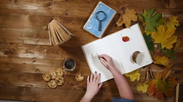 Otoño concepto vista superior. Libros, hojas de arce, té en la vieja mesa de madera. Mujer escribiendo notas en el cuaderno — Vídeos de Stock