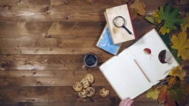 Sonbahar konsepti üstten görünüm. Kitaplar, akçaağaç yaprakları, eski ahşap tabloda çay. Not defterinde yazma kadın