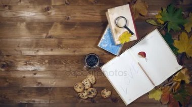 Sonbahar konsepti üstten görünüm. Kitaplar, akçaağaç yaprakları, eski ahşap tabloda çay. Not defterinde yazma kadın