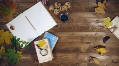 Sonbahar konsepti üstten görünüm. Kitaplar, akçaağaç yaprakları, eski ahşap tabloda çay. Not defterinde yazma kadın