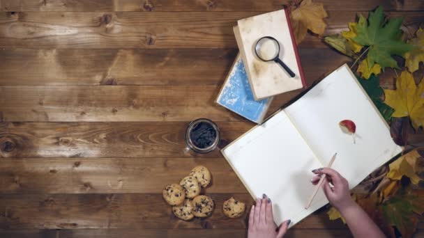 Otoño concepto vista superior. Libros, hojas de arce, té en la vieja mesa de madera. Mujer escribiendo notas en el cuaderno — Vídeo de stock