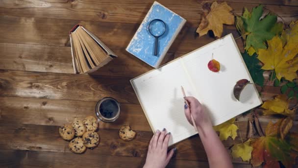 Otoño concepto vista superior. Libros, hojas de arce, té en la vieja mesa de madera. Mujer escribiendo notas en el cuaderno — Vídeos de Stock