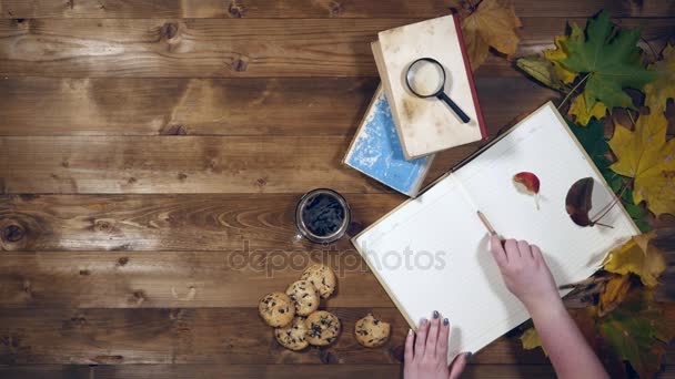 Φθινοπωρινή θέα πάνω έννοια. Βιβλία, φύλλα σφενδάμου, τσάι στο παλιό ξύλινο τραπέζι. Γυναίκα γράφει σημειώσεις στο Σημειωματάριο — Αρχείο Βίντεο