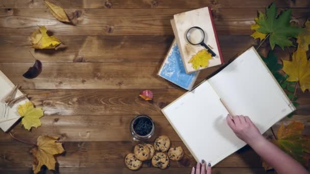 Otoño concepto vista superior. Libros, hojas de arce, té en la vieja mesa de madera. Mujer escribiendo notas en el cuaderno — Vídeos de Stock