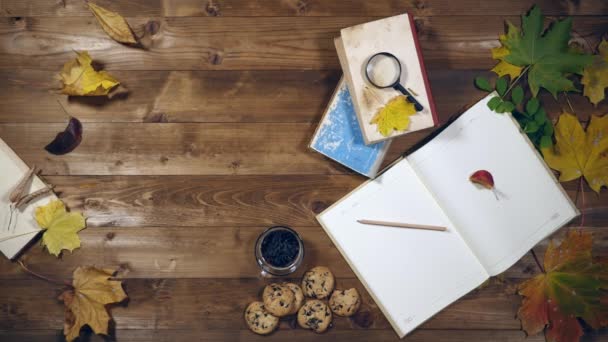 Autumn concept top view. Books, maple leaves, tea on the old wooden table. Woman writing notes in the notebook — Stock Video