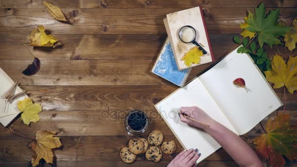 Otoño concepto vista superior. Libros, hojas de arce, té en la vieja mesa de madera. Mujer escribiendo notas en el cuaderno — Vídeos de Stock