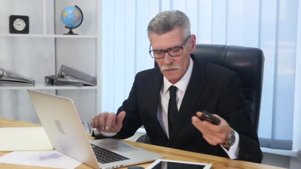 Старший чоловік розмовляє з білим смартфоном в офісі — стокове відео