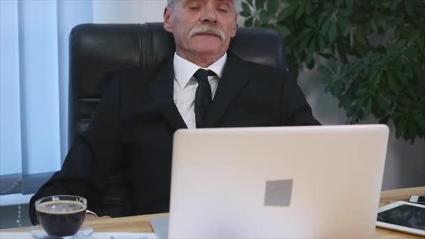 Старий бізнесмен нахилився назад у своє офісне крісло, він посміхається і мріє — стокове відео