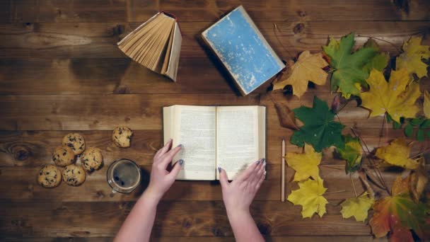 Вид зверху на осінню концепцію. Книги, кленове листя, чай на старому дерев'яному столі. Жінка пише нотатки в блокноті — стокове відео