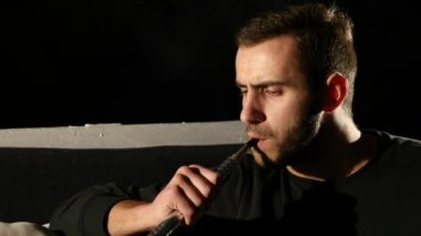 Genç sakallı adam siyah arka plan üzerine bir nargile closeup içiyor. ağır çekim