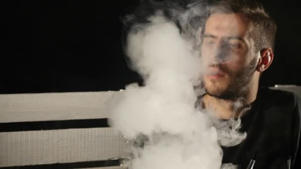 El joven fuma una cachimba solo sobre fondo negro — Vídeos de Stock