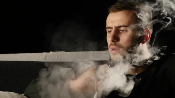 O jovem fuma um narguilé sozinho no fundo preto — Vídeo de Stock