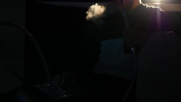 Tânărul fumează narghilea și lasă inelele de fum într-o cameră întunecată aproape — Videoclip de stoc