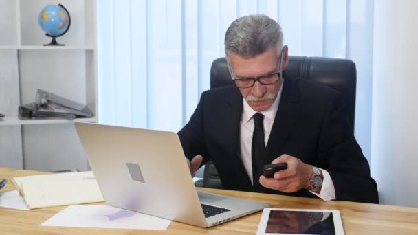 Homem sênior fala com smartphone branco no escritório — Vídeo de Stock