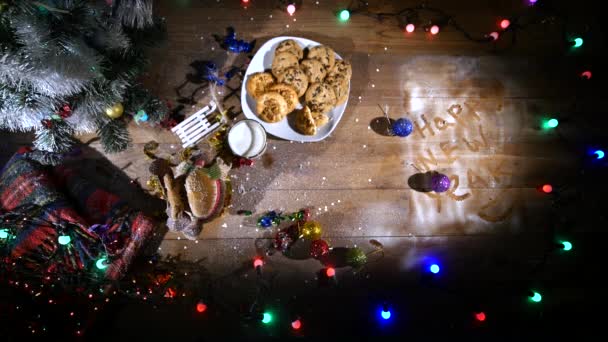 Fából készült barna asztal díszített koszorúkat és karácsonyi cucc. Egy pohár tej és a cookie-kat a karácsonyi asztal egy tányér — Stock videók