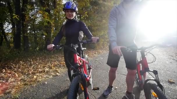 Attraktives Paar, das mit Fahrrädern im Herbstpark spazieren geht. Sonnenlicht. Zeitlupe — Stockvideo