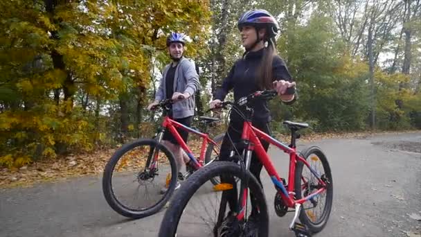 Attraktives Paar, das mit Fahrrädern im Herbstpark spazieren geht. Zeitlupe — Stockvideo