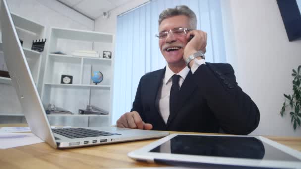 Senior man met witte smartphone spreekt en glimlacht in kantoor — Stockvideo