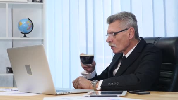 Forretningsmann drikker kaffe mens han ser på PC-skjermen. – stockvideo