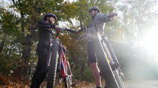 Attraktivt par promenader med cyklar i parken hösten. solljus bakgrund. slowmotion — Stockvideo