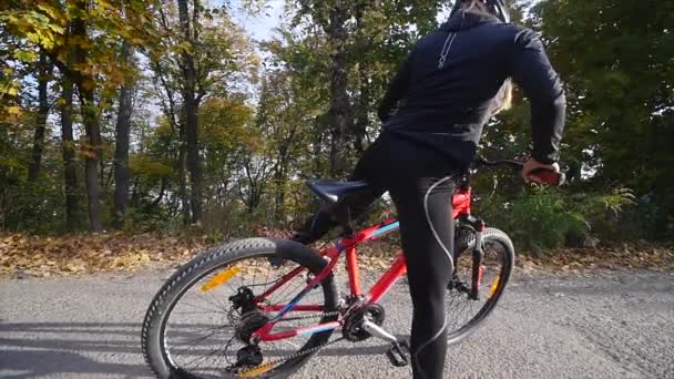 Feche o tiro da jovem mulher em uma bicicleta no parque de outono. câmara lenta — Vídeo de Stock