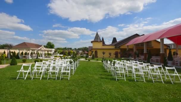 Bruiloft gangpad decor. Witte bruiloft stoelen. De ceremonie van het huwelijk van de buitenlucht. Bruiloft ingesteld in de tuin. Zonnige dag — Stockvideo