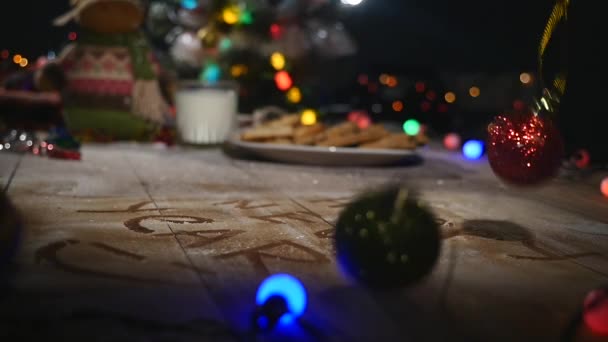 Table en bois marron décorée avec des trucs de Noël et des guirlandes. Un verre de lait et une assiette de biscuits sur une table de Noël — Video