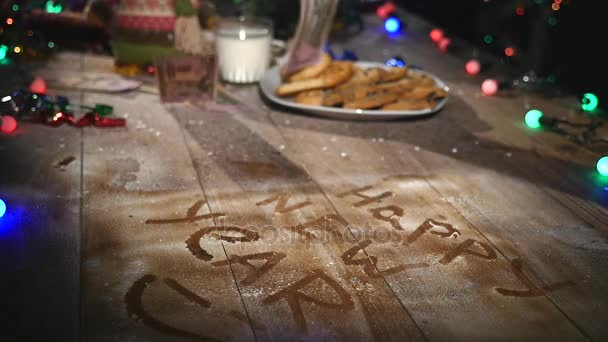 Hölzerner brauner Tisch mit weihnachtlichem Zeug und Girlanden dekoriert. Ein Glas Milch und ein Teller Plätzchen auf dem Weihnachtstisch. Geld fällt auf den Tisch — Stockvideo