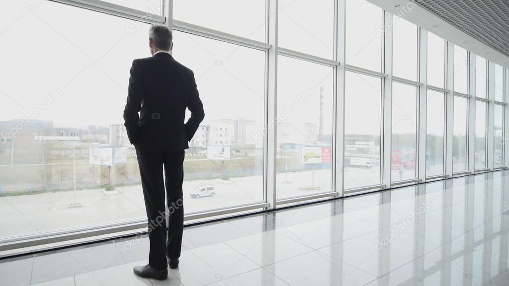 Man come and stand at full height, gaze out airport terminal window