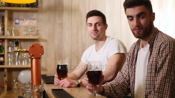 Dua pemuda teman duduk di bar dan berbicara satu sama lain sambil minum bir — Stok Video
