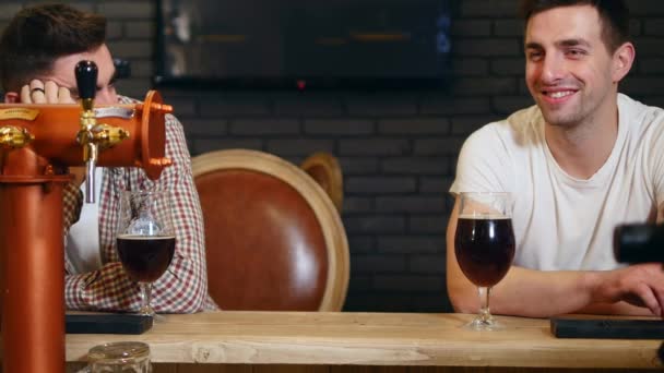 Dwóch młodych mężczyzn przyjaciół siedzi barze i rozmawiać ze sobą podczas picia piwa — Wideo stockowe