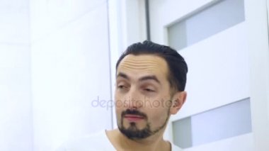 Yakın çekim. Adam aynanın önünde yıkar. Beyaz bir T-shirt yorgun tıraşsız adam