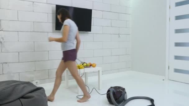 Μια νεαρή κοπέλα είναι ο καθαρισμός το σπίτι χρησιμοποιώντας μια ηλεκτρική σκούπα — Αρχείο Βίντεο