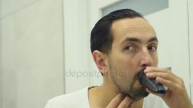 Genç adam banyoda Elektrikli tıraş makinesi ile sakalını tıraş